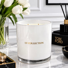 A white scented candle in a clear glass jar with gold 'LV COLLECTION' lettering, styled on a marble surface with white tulips, a reed diffuser, and a Tom Ford box in the background.