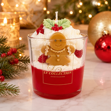 A festive Christmas-themed candle from LV Collection in a clear glass jar. The candle features a deep red wax base, topped with white whipped cream, a gingerbread man figure, green holly leaves, and red berries.